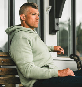 Man sitting on bench in Kilo Lite Hoodie Jade nav CTA