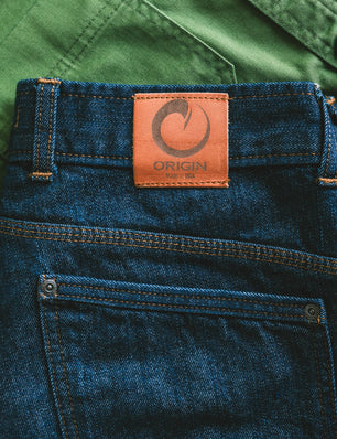 Close-up of blue jeans with a brown leather label on a green background