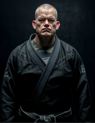 Person wearing a black martial arts uniform with a black belt against a dark background