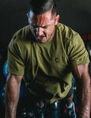 Man in a green t-shirt exercising on a bike in a gym setting